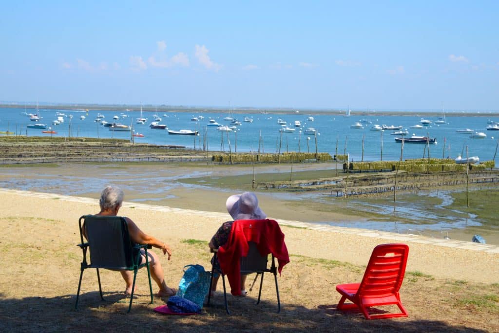 Immobilier en Gironde. Envie d’acheter au bord de l’Atlantique ? Le palmarès des communes les moins chères… et des plus chics ! Couple assis devant un parc d'huîtres dans le Bassin d'Arcachon